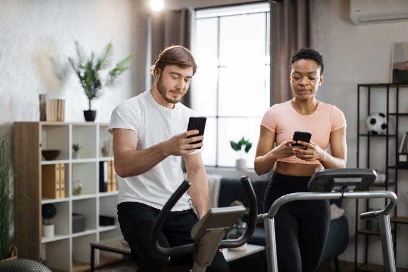 Przeglądanie social mediów na maszynach do cardio mężczyzna i kobieta przeglądają smartfony zamiast ćwiczyć