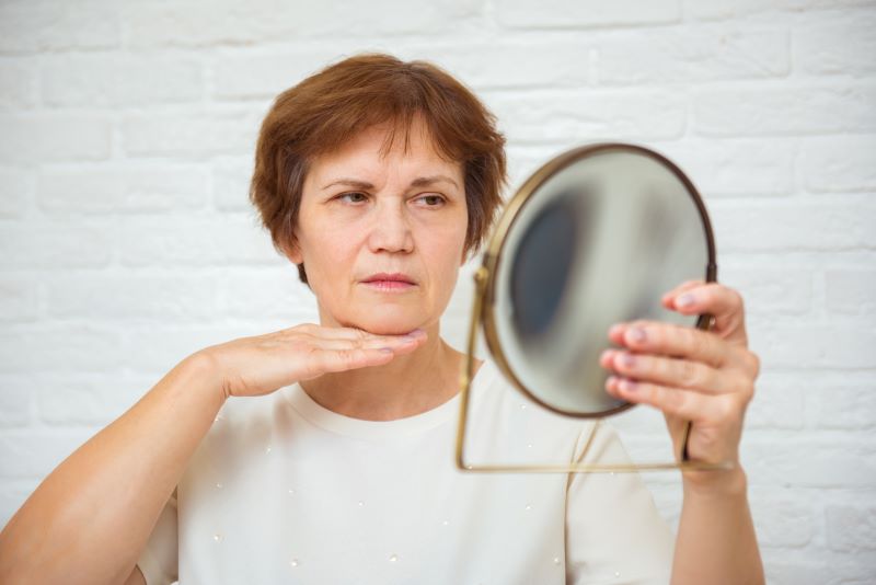 dojrzała kobieta sprawdzająca swój podwójny podbródek w lustrze
